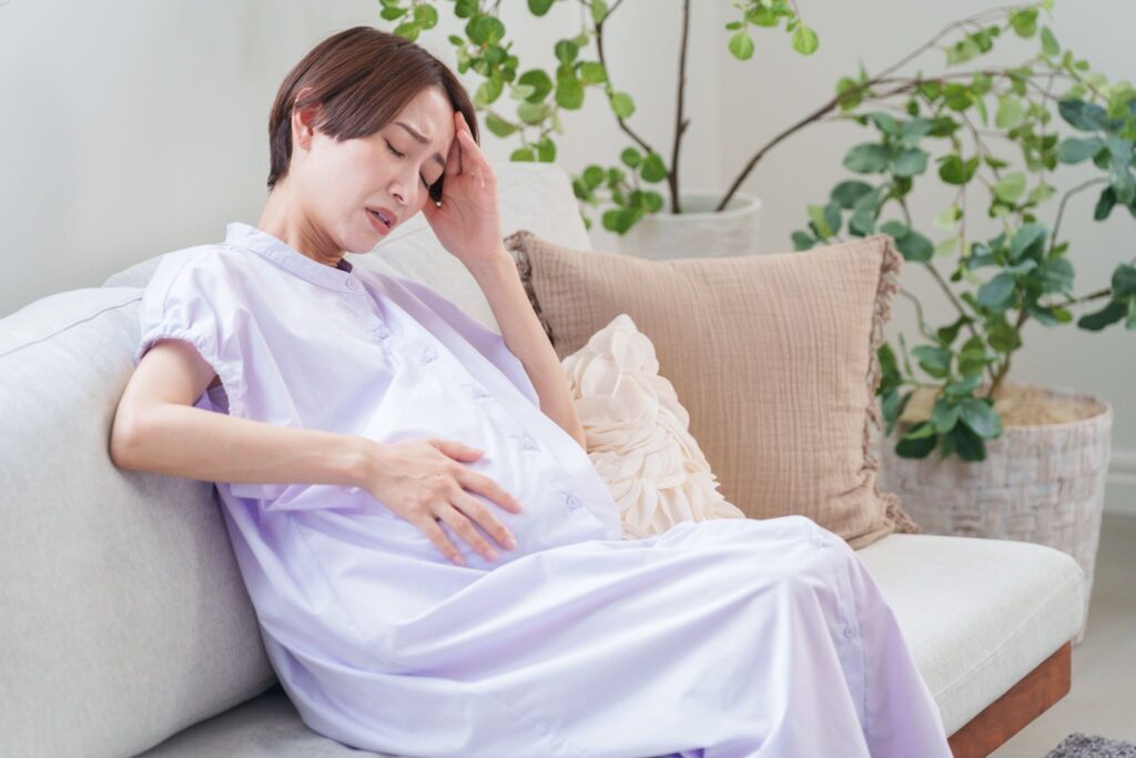高齢で妊娠した女性。ソファに座りお腹を押さえている