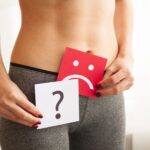 お腹の前で困った顔とはてなマークの紙を見せている女性
