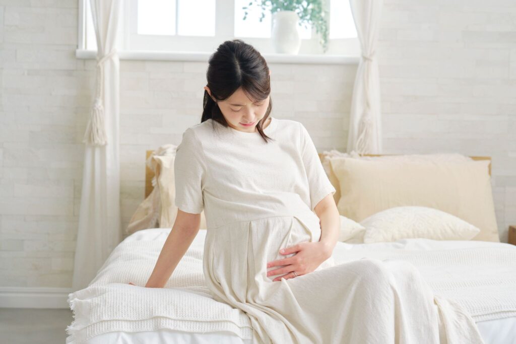 ベッドに座ってお腹を押さえている妊婦