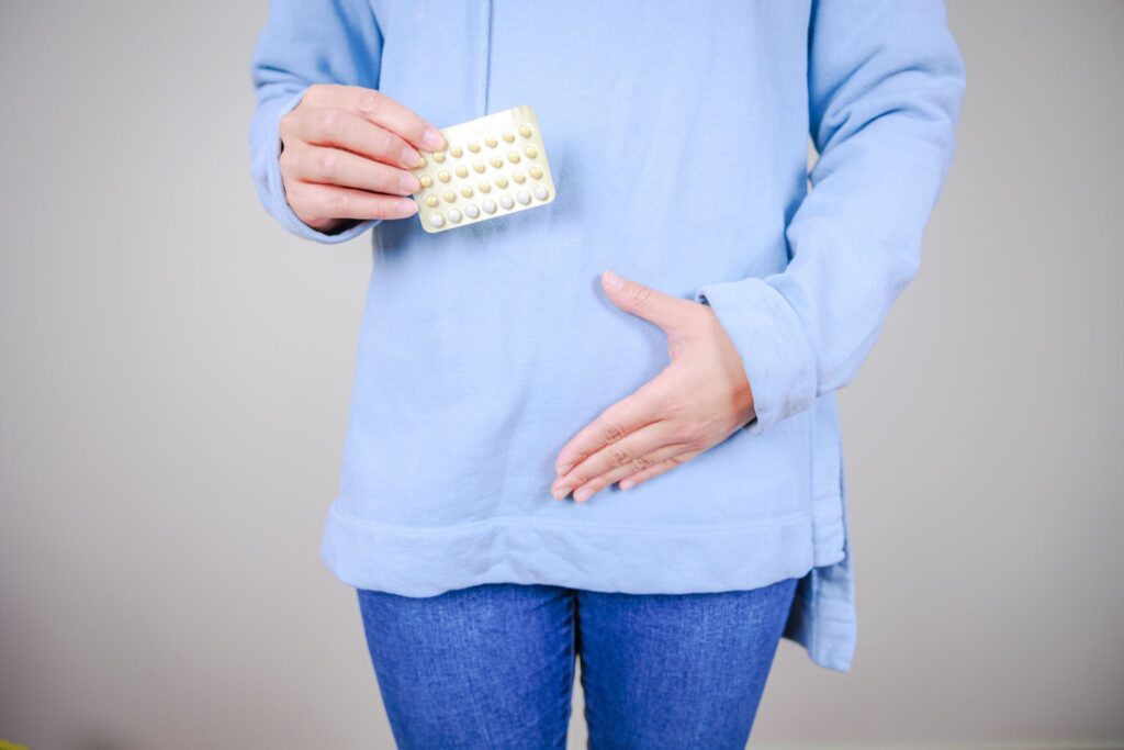 ピルを持った女性。片手をお腹に当てている