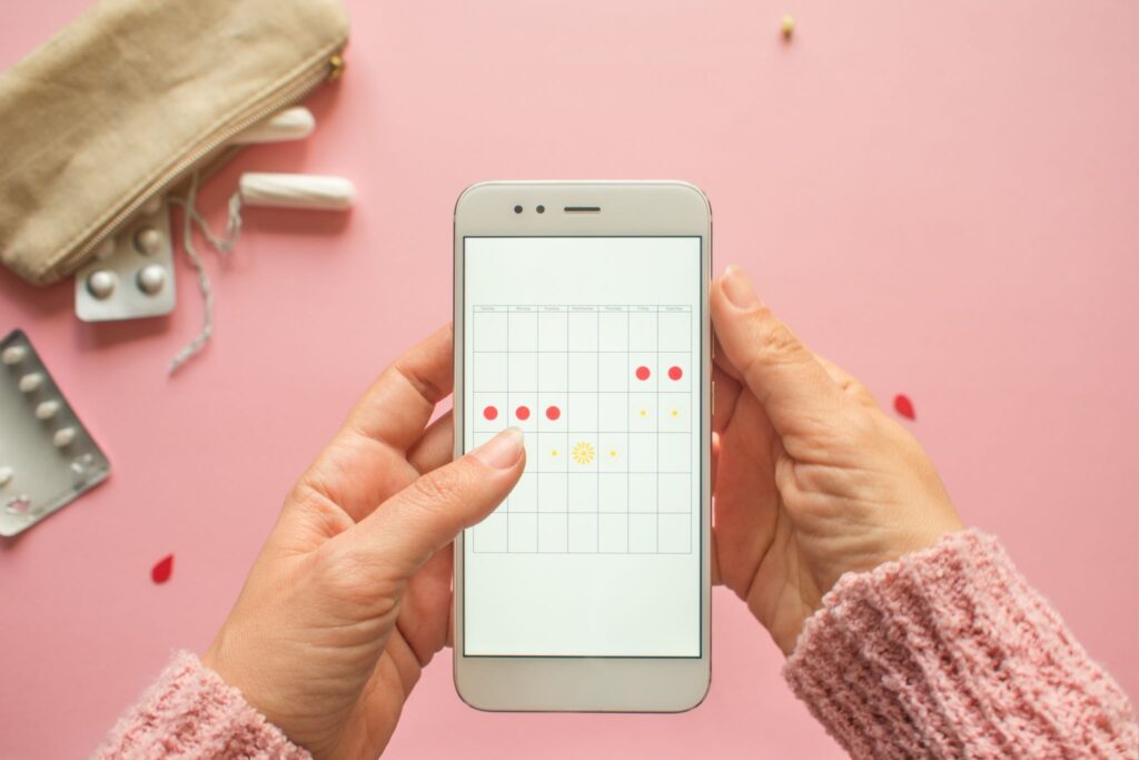 スマホで生理周期をチェックしている女性。背景に薬とタンポン