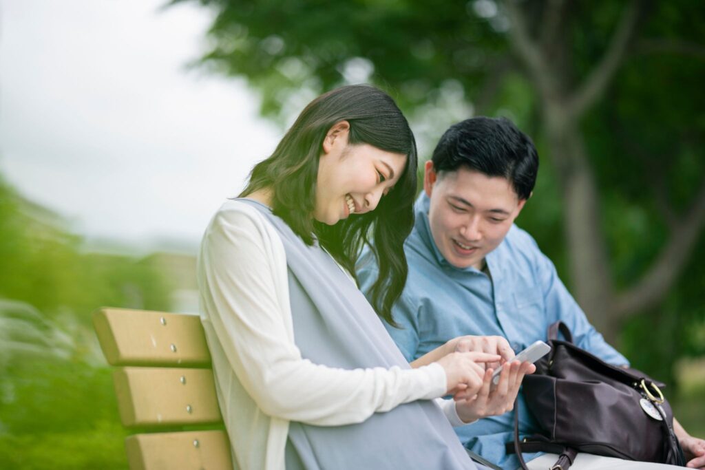 ベンチに座ってスマホを見ている妊婦と夫
