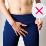 バツマークを持って下腹部を押さえている女性