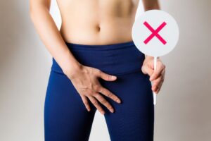 バツマークを持って下腹部を押さえている女性