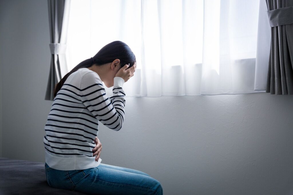 片手でお腹を押さえてもう片方の手で頭を押さえている女性