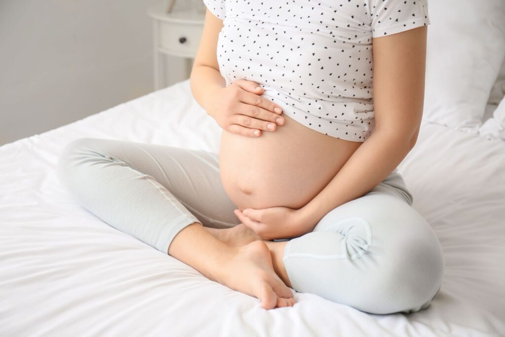 ベッドの上でお腹に触れている妊婦