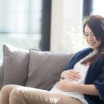 ソファに座ってお腹に触れている妊婦