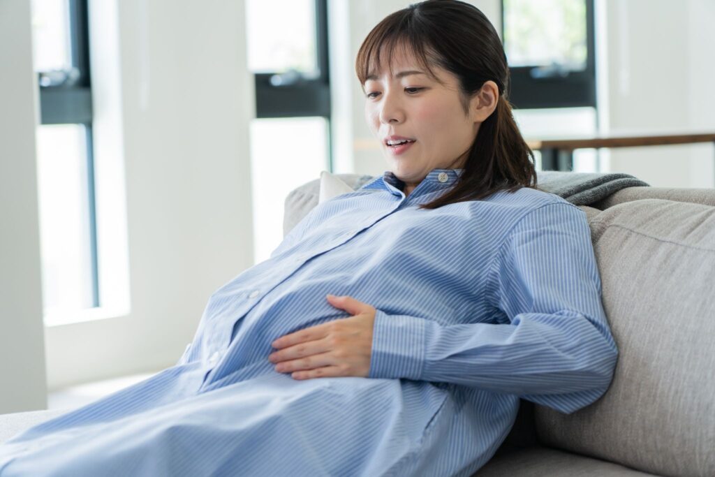 ソファに座ってお腹に触れている妊婦