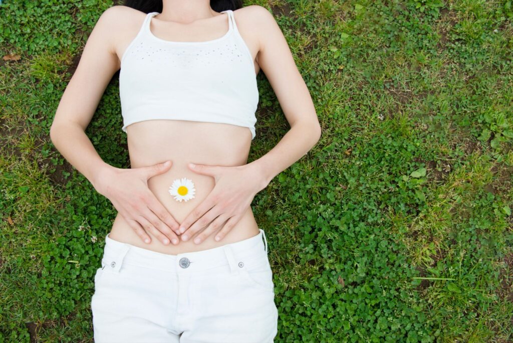 芝生に寝転がってお腹に手を当てている女性